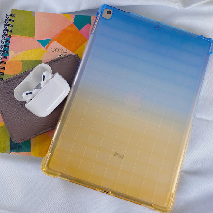 A transparent-colored silicone case with corner-bumpers covering the back of an Apple iPad. The top-half blue blends to the yellow-colored bottom-half. #color_blue-yellow