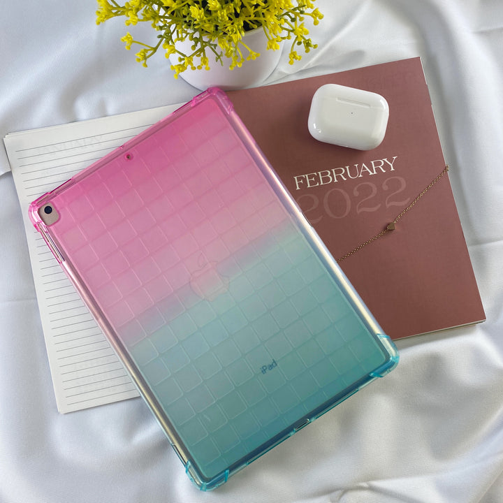 A transparent-colored silicone case with corner-bumpers covering the back of an Apple iPad. The top-half pink blends to the teal-colored bottom-half. #color_pink-green