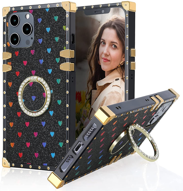A box-shaped, TPU, iPhone 12 Pro Max case, with gold corner bumpers and gold rivets on its black trim. The case’s back is designed black, with rainbow hearts, and glitter. A gold trim ring, with diamond studs, doubles as a handle and kickstand for the case. #color_black-glittery-hearts