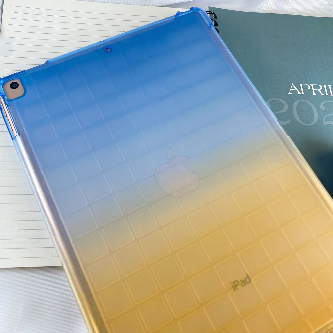 A transparent-colored silicone case with corner-bumpers covering the back of an Apple iPad. The top-half blue blends to the yellow-colored bottom-half. #color_blue-yellow