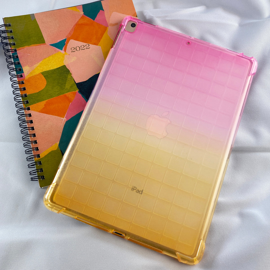 A transparent-colored silicone case with corner-bumpers covering the back of an Apple iPad. The top-half pink blends to the yellow-colored bottom-half. #color_pink-yellow